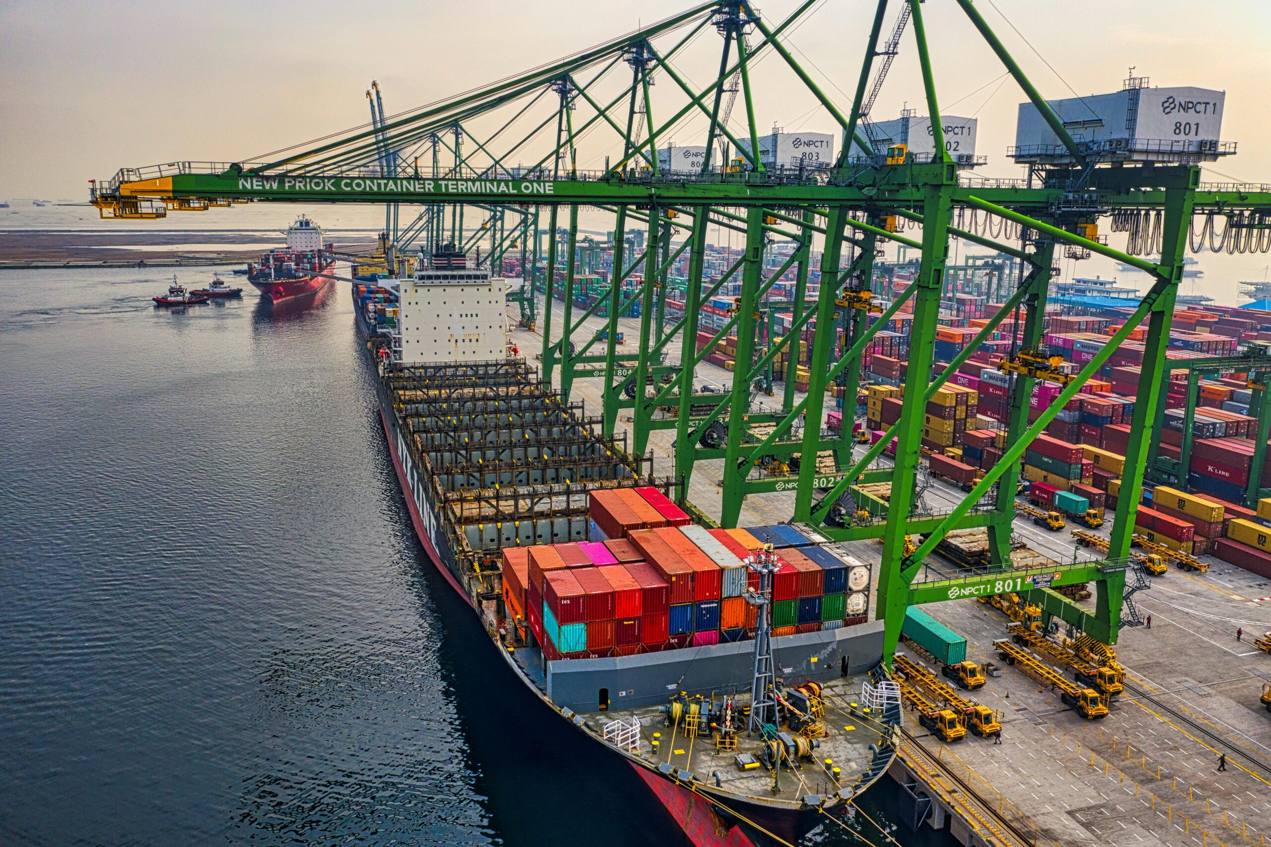 Aerial view of a cargo ship docked at New Priok Container Terminal, Jakarta, showcasing vibrant logistics activity.